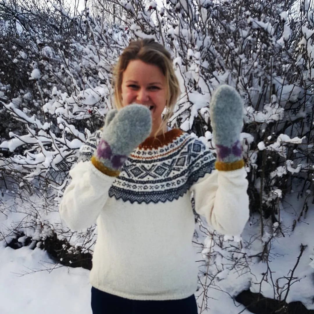 Tine holder opp et par lysegrå sauevotter foran ansiktet ute i snøen, og ler.