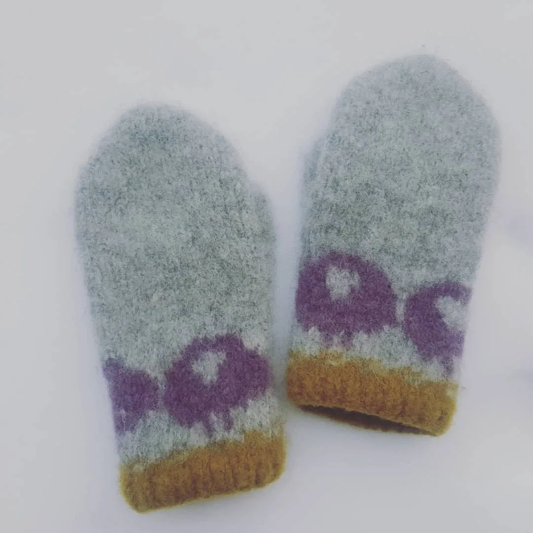 Et par lysegrå sauevotter med lilla sauer og okerfarget kant, lagt ned i snøen.