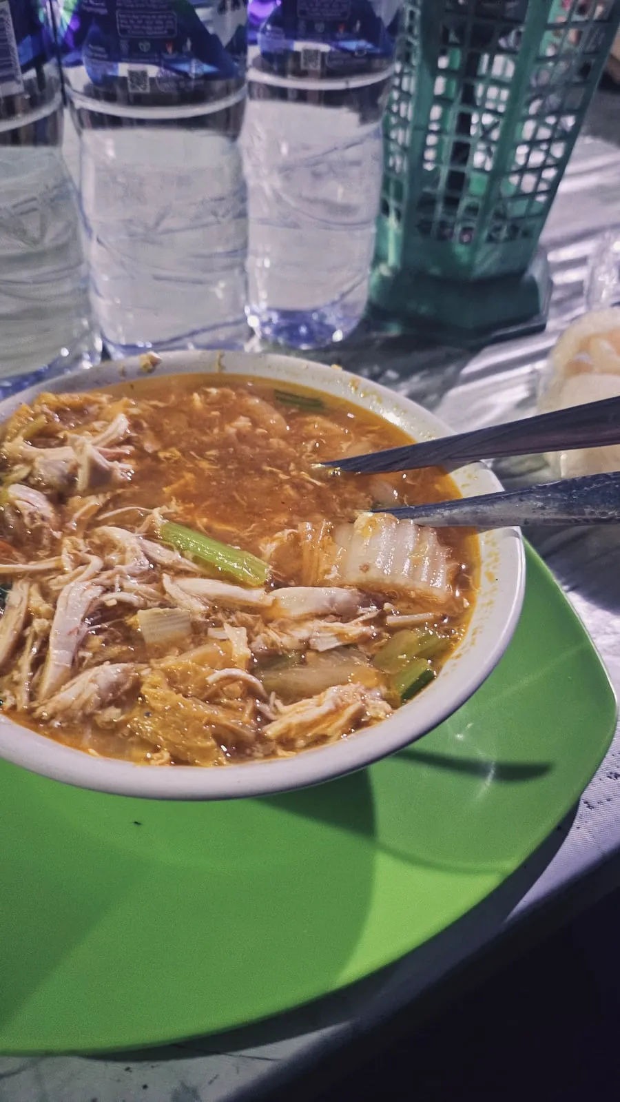 En dyp skål med suppe, kylling og grønnsaker på et grønt brett.